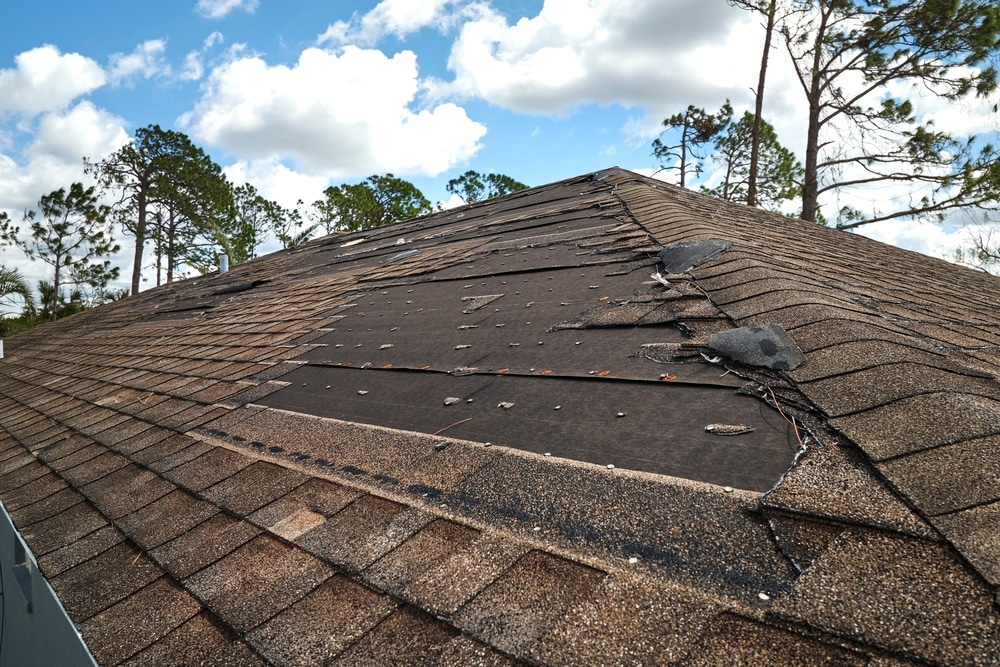 Wind damaged house roof with missing asphalt shingles after hurricane Ian in Florida. Repair of home rooftop concept