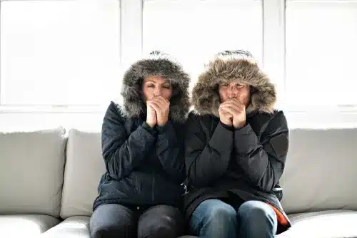 A couple sitting inside on their couch wearing coats