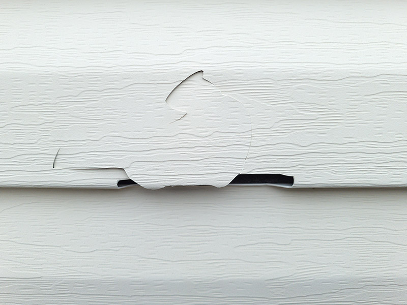 Siding panel with a broken and cracked section requiring repair.