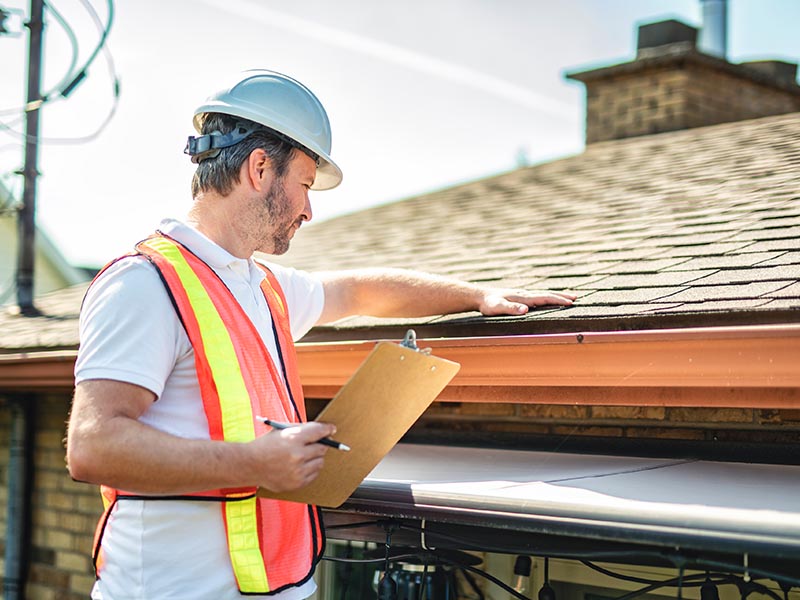 Roofer holding a clip board and inspection a residential roof from on a ladder.